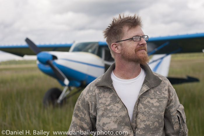 Portrait of Chet Harris and his Maule M5 airplane in a tall grass field, Alaska